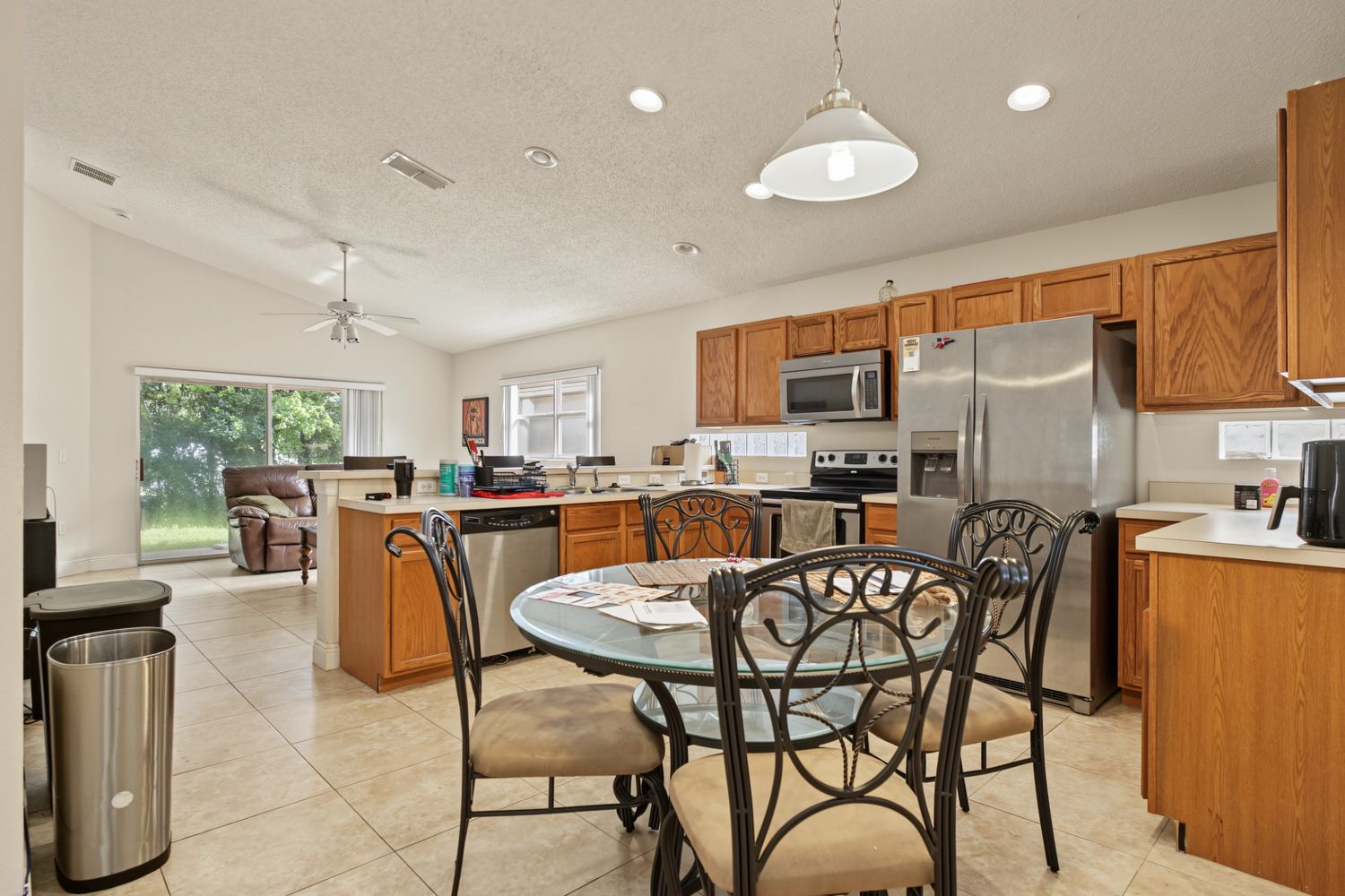 Original: the same kitchen with cluttered counters, paperwork on the table and a recliner in the living area